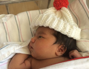 A local newborn models his special birthday gift: a hand-knit caps crafted by the Twin Cities Community Hospital volunteer knitters.