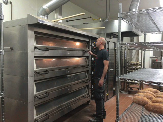 Back Porch Bakery owner Bill Brocco checks artisan bread in one of the ovens in the Carlton Hotel bakery. Photo by Heather Young